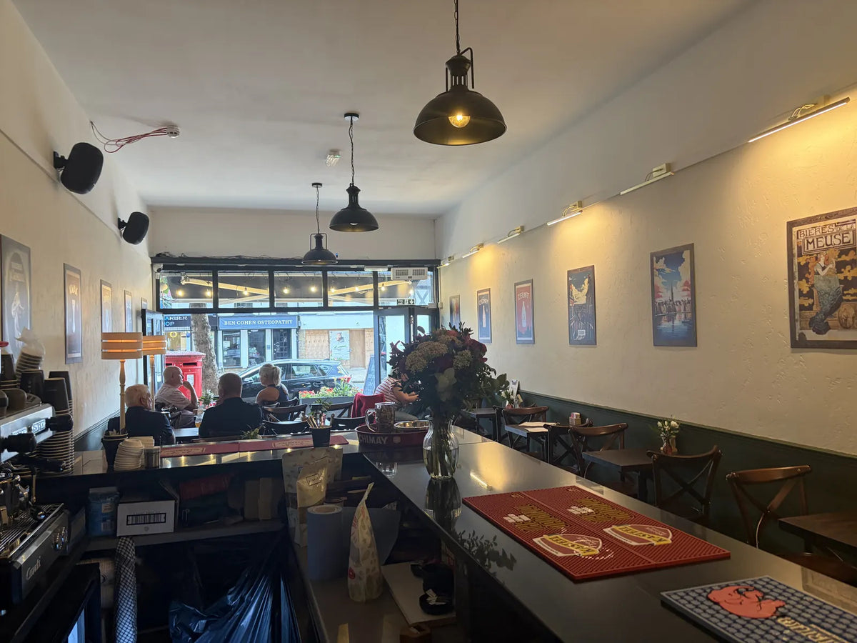 Looking down the Epping café bar towards the glazed front, with poster-lined walls, flowers on the bar and a few guests by the window