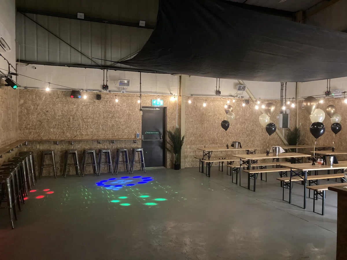 The Stortford event hall set for a party: beer-hall benches, festoon lights, black and gold balloons and disco lights on the floor