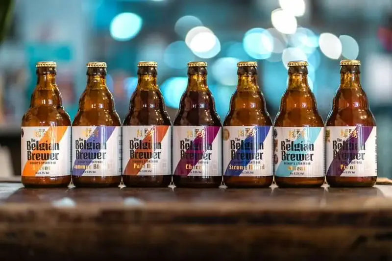 Seven bottles of The Belgian Brewer house beers lined up on a bar, each label with its own coloured stripe
