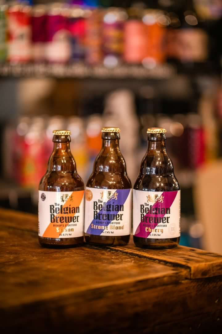 Three bottles of The Belgian Brewer beer on a wooden bar: Saison, Strong Blond and Cherry
