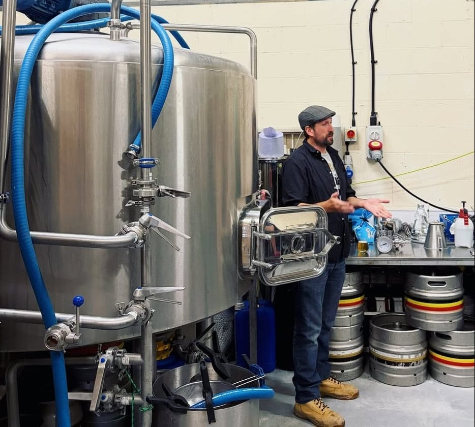 Head brewer Darren Lawrence talking visitors through the brewhouse on a brewery tour, with kegs stacked behind him