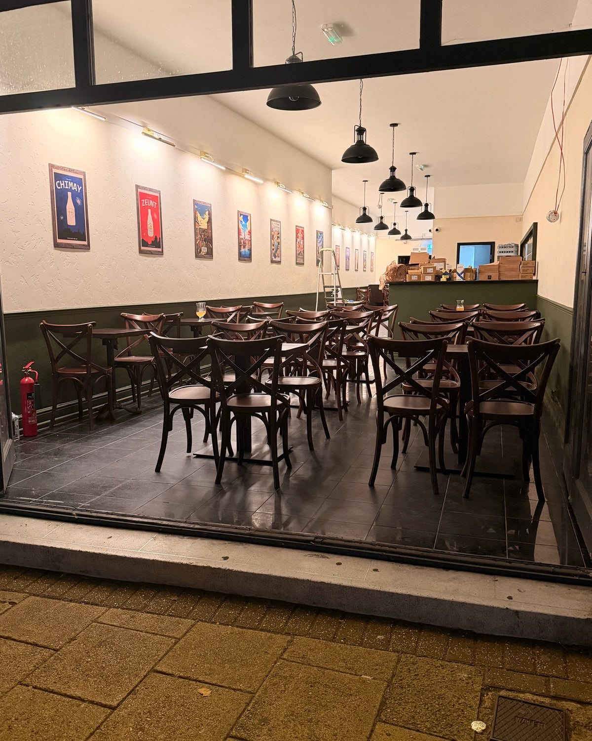 The Belgian café in Epping seen from the High Street at night, with bentwood chairs and Belgian beer posters inside