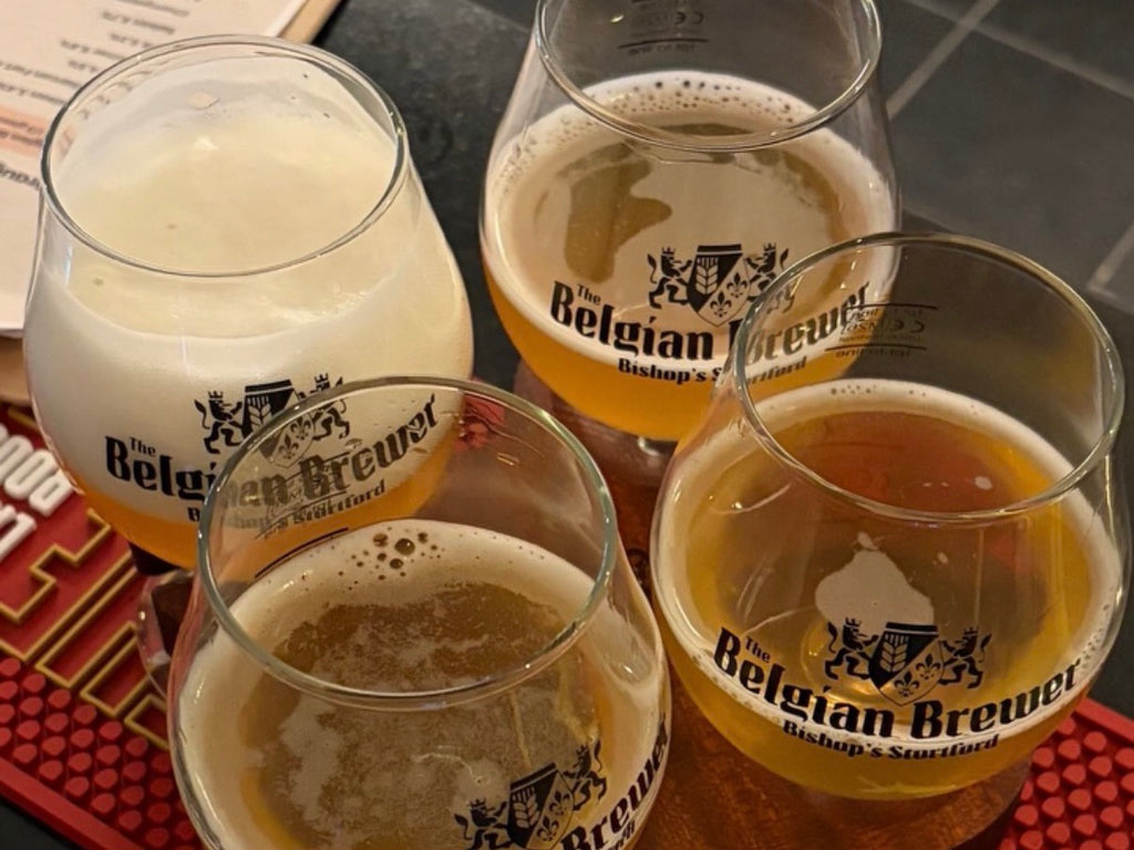 A flight of four Belgian Brewer beers in crested tasting glasses on a wooden paddle