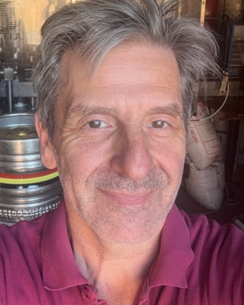 Nik Lemmens, The Belgian Brewer, in the brewery with kegs and the bottling line behind him